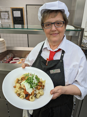 Mitarbeiterin der Mensa hält ein Pasta-Gericht in die Kamera | Foto: StwH